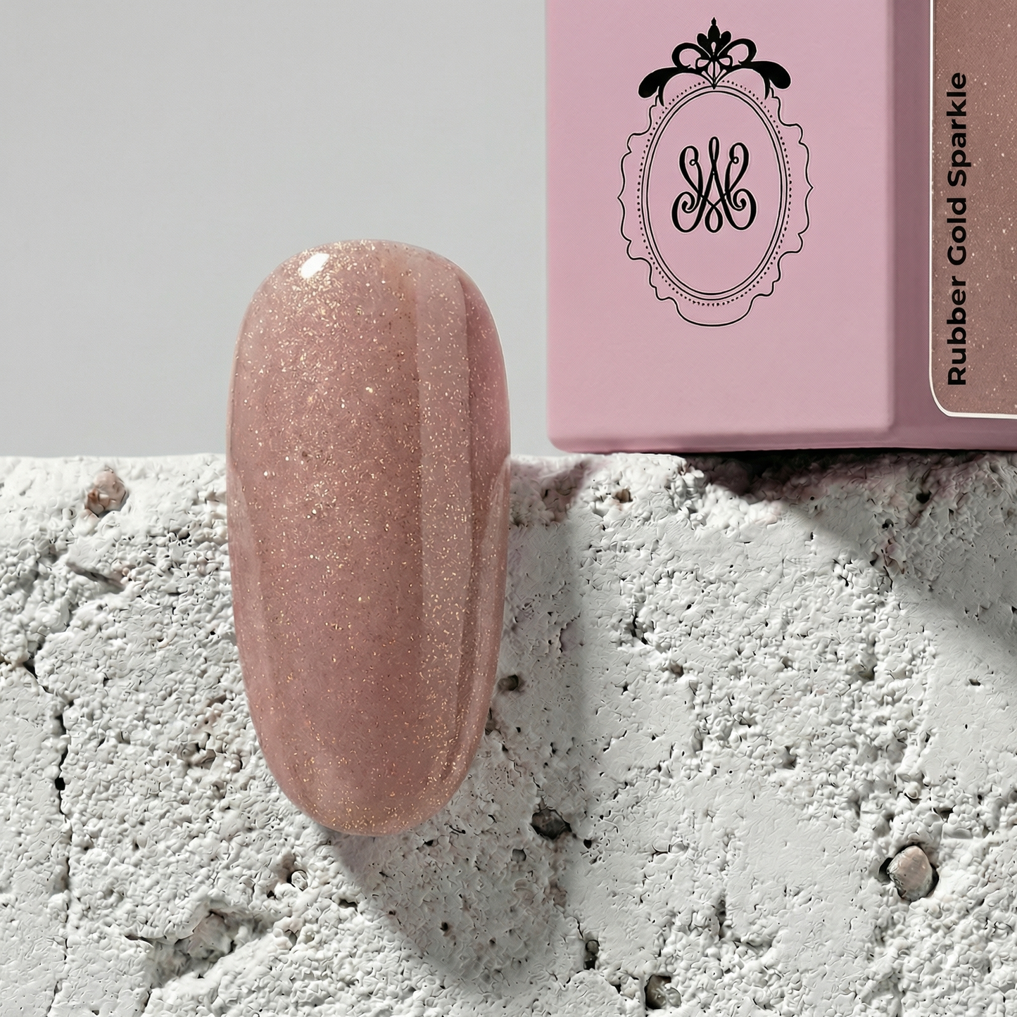 Professionelle Produktaufnahme des Soak-Off Gels „Rubber Gold Sparkle“. Zu sehen ist ein hochglänzender Nageltip in einem zarten Nude-Rosa mit feinen Gold-Glitzerpartikeln, platziert vor einer hellrosa Flasche mit elegantem Logo auf einer strukturierten, weißen Betonoberfläche.