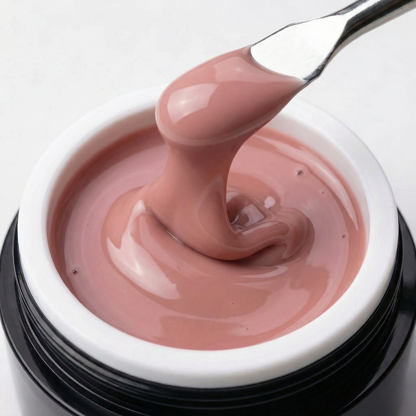 Ein offener Tiegel des Studio Amelie „Timeless“ Gels mit einem Spatel, der einen dicken Tropfen des viskosen, selbstglättenden Nude-Rosé-Gels hochzieht, um die Konsistenz zu zeigen.