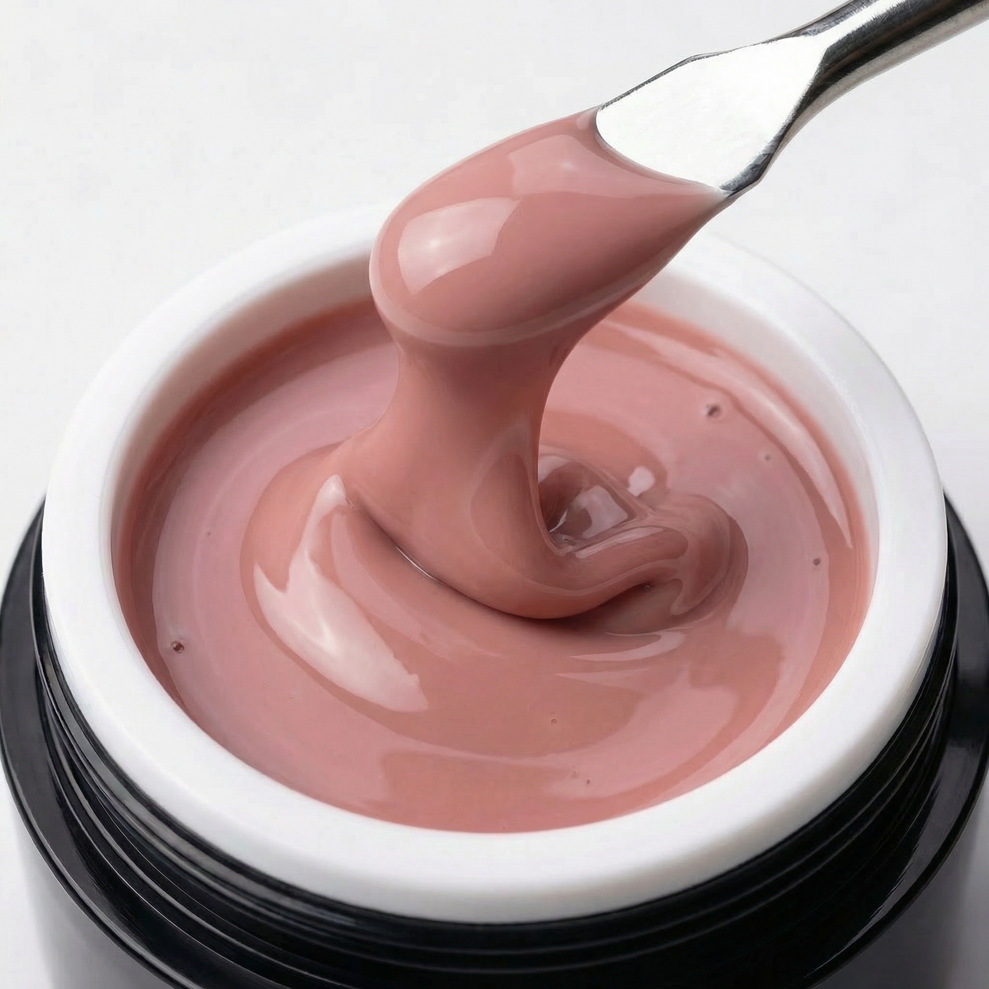 Ein offener Tiegel des Studio Amelie „Timeless“ Gels mit einem Spatel, der einen dicken Tropfen des viskosen, selbstglättenden Nude-Rosé-Gels hochzieht, um die Konsistenz zu zeigen.