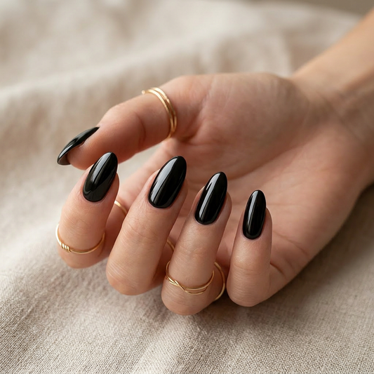 Hand mit goldenen Ringen und mandelförmigen Nägeln in glänzendem Schwarz, versiegelt mit Repair Top Gel No Wipe von Studio Amelie